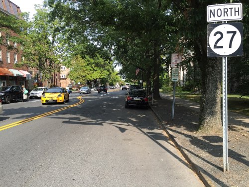 A street scene showing cars parked along the road, with a sign indicating "North 27" and trees lining the sidewalk.