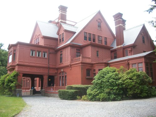 A large red Victorian-style mansion surrounded by greenery and gravel pathways.