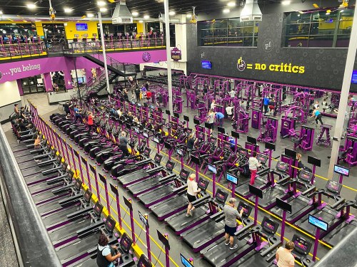 A spacious gym filled with people using treadmills and exercise equipment, featuring purple and black decor.