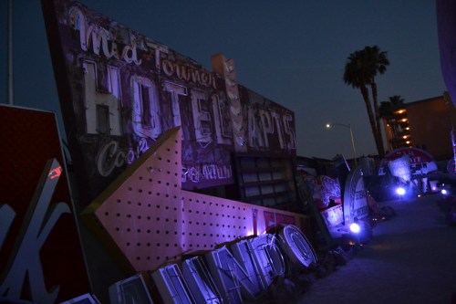 Neon-lit vintage hotel signs at dusk, with palm trees and a dimly lit pathway.