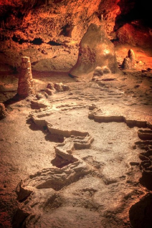 A dimly lit cave interior featuring unique rock formations and textured ground, illuminated by warm, natural light.