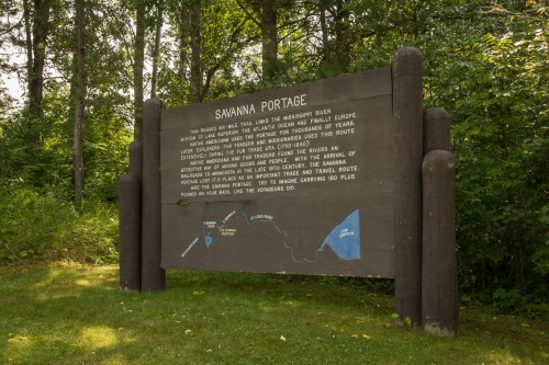 Sign for Savanna Portage, detailing its historical significance and route along the Mississippi River, surrounded by trees.