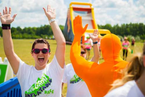 A woman in a white shirt cheers with her arms raised, while a person in an orange suit waves behind her at an inflatable race.