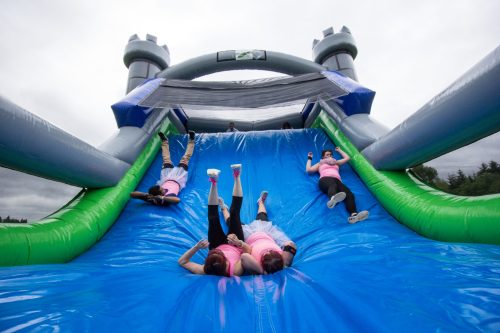 A group of people in pink shirts sliding down a large inflatable slide at an outdoor event.