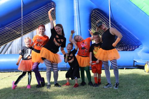 A group of children and adults in Halloween costumes, wearing orange tutus and striped leggings, posing playfully outdoors.