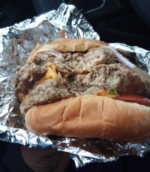 A hand holding a large, foil-wrapped burger with cheese, lettuce, tomato, and onion.