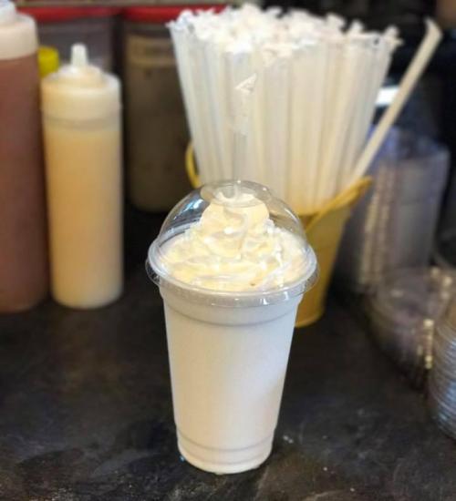 A tall cup of milkshake topped with whipped cream and a straw, set against a backdrop of condiments and straws.