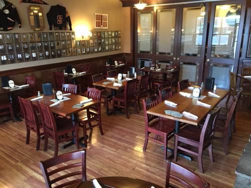 A cozy restaurant interior with wooden tables, chairs, and framed photos on the walls, set for dining.