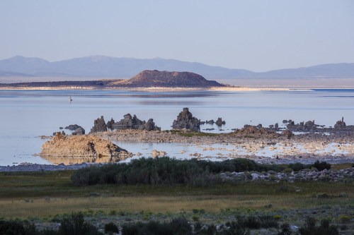 A serene landscape featuring a calm lake with rocky formations and distant mountains under a clear sky.