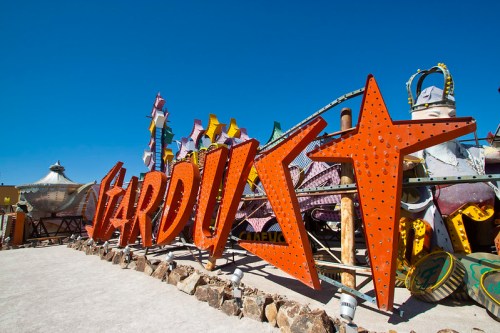 Colorful vintage neon signs, including "Stardust," displayed outdoors against a clear blue sky.