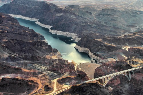 Aerial view of a river surrounded by mountains, featuring a dam and a bridge in the foreground.