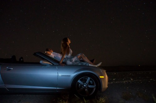 A couple relaxes in a silver convertible under a starry night sky, enjoying the serene atmosphere.
