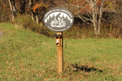 Sign for "Lodging in the Mountains" with a cyclist graphic, surrounded by trees and grass.