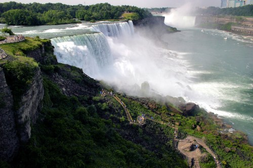 Aerial view of Niagara Falls, showcasing cascading water and lush greenery along the riverbank.
