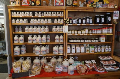 A wooden shelf filled with jars and bottles of maple syrup, candies, and various local products.