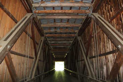 View of the interior of a wooden covered bridge, showcasing its beams and structure, leading to bright light at the end.