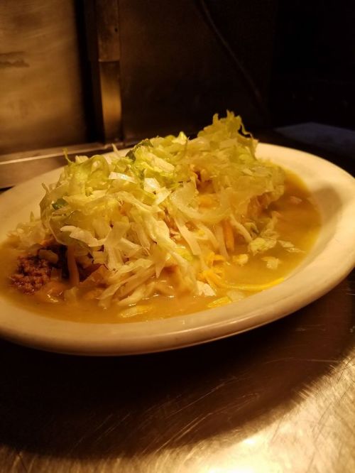 A plate of food featuring a savory mixture topped with shredded lettuce and cheese, served in a warm sauce.