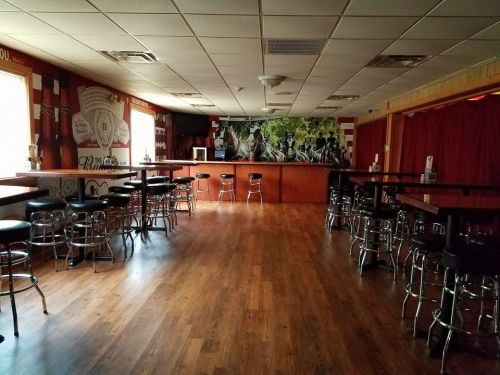 A spacious, empty bar with wooden floors, high tables, and a mural on the wall, featuring red and white decor.