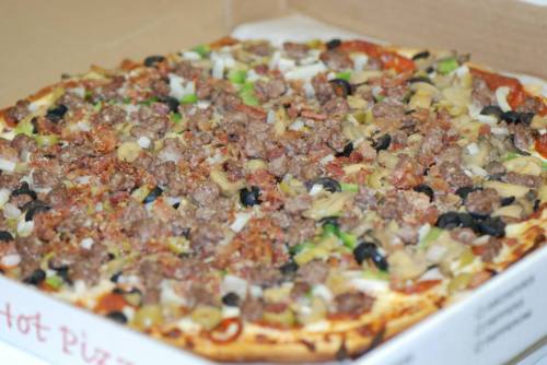 A close-up of a pizza topped with ground meat, olives, green peppers, onions, and mushrooms in a pizza box.