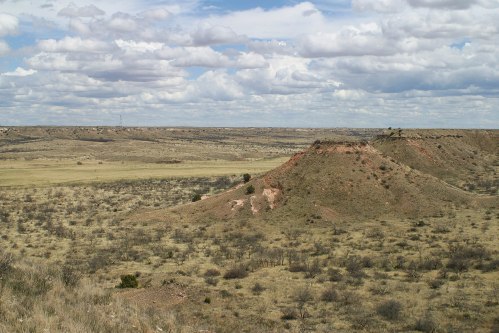 A vast landscape featuring rolling hills, sparse vegetation, and a cloudy sky in a rural setting.