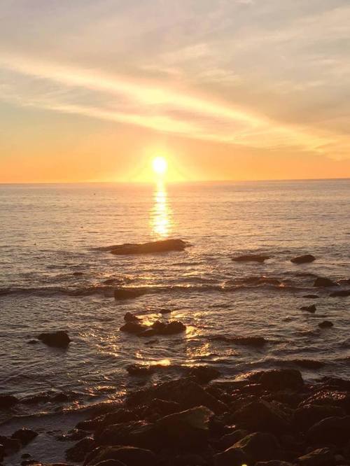 Sunset over a calm ocean, with golden light reflecting on the water and rocky shoreline.