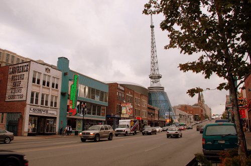 A street view featuring colorful buildings, a record store, and a tall radio tower under a cloudy sky.