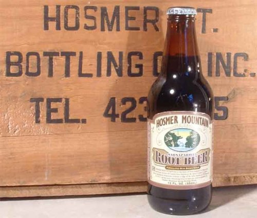 A vintage bottle of Hosmer Mountain Root Beer in front of a wooden crate with the company's name and contact details.