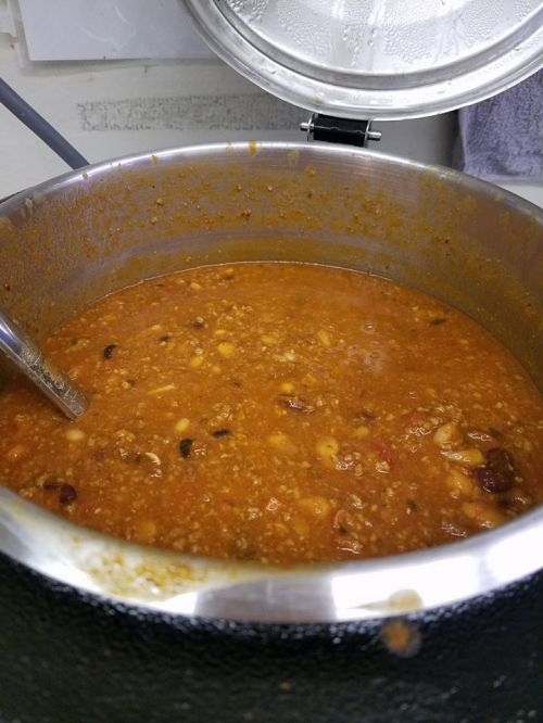 A large pot filled with thick, hearty chili, featuring beans and meat, with a metal ladle resting inside.