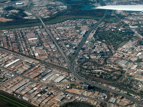 Aerial view of a cityscape with highways, industrial areas, and green spaces, seen from an airplane window.