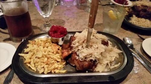 A metal platter with sauerkraut, meat, and a side of crispy noodles, accompanied by a small dish of red sauce.