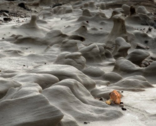 A textured landscape of smooth, sculpted rock formations with a small orange object in the foreground.