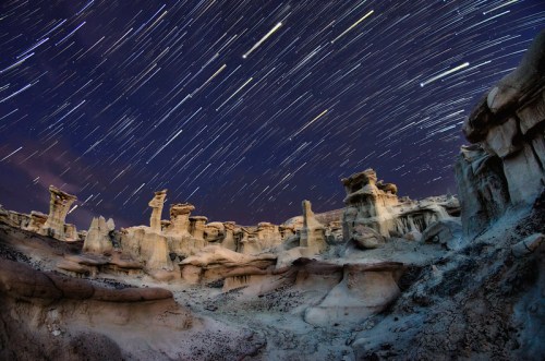 Star trails illuminate a rugged, otherworldly landscape of rock formations under a night sky.