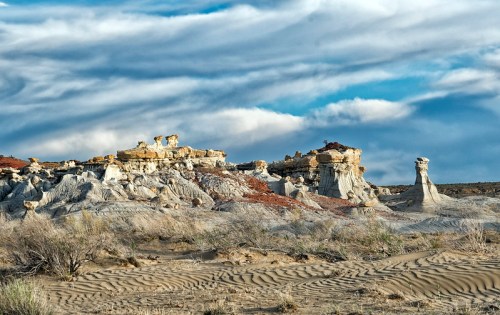 A rugged landscape featuring unique rock formations under a cloudy sky, with sandy terrain in the foreground.