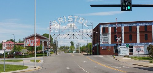 Sign welcoming visitors to Bristol, with buildings and a clear blue sky in the background. Traffic light visible.