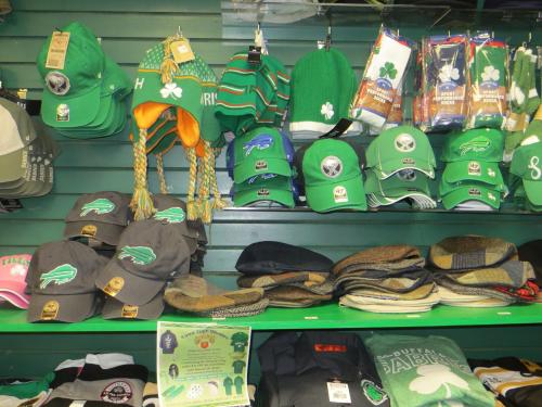A display of green hats, scarves, and apparel, featuring sports team logos and St. Patrick's Day themes.