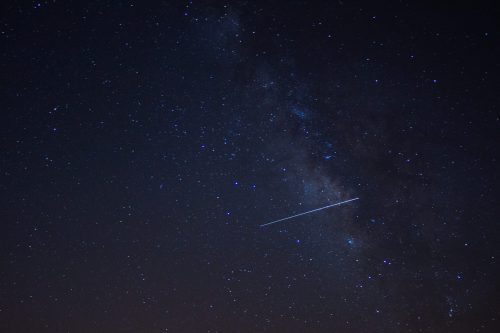 A starry night sky featuring the Milky Way and a bright meteor streaking across the scene.