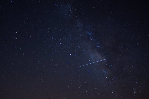 A starry night sky featuring the Milky Way and a bright meteor streaking across the scene.