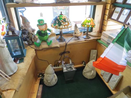 A cozy display featuring a leprechaun, decorative lamps, and Italian flag, surrounded by whimsical garden gnomes.