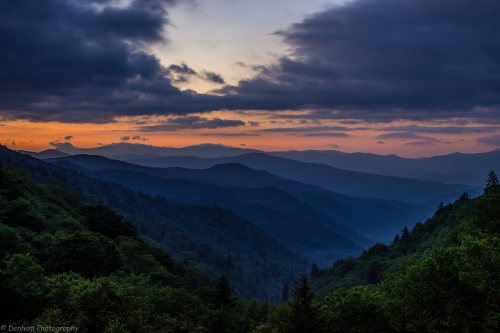A scenic view of layered mountains at sunset, with dramatic clouds and a soft gradient of colors in the sky.