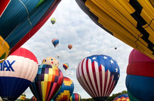 A vibrant scene of colorful hot air balloons in the sky, with various patterns and designs against a cloudy backdrop.