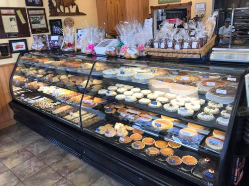 A display case filled with various baked goods, including pies, pastries, and cookies, in a cozy bakery setting.