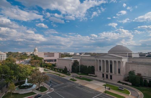 A view of a cityscape featuring a museum, fountain, and clouds, with a distant dome-shaped building.