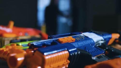A close-up of a colorful Nerf blaster with blurred toy guns in the background.