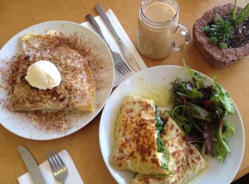 A plate with a dessert crepe topped with ice cream, alongside a cheesy omelet and a fresh salad, with a drink in a jar.
