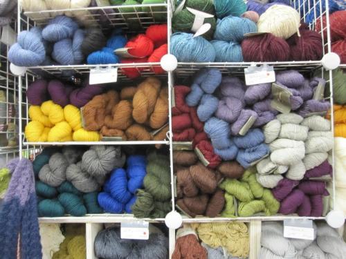 A colorful display of various yarn skeins organized on shelves, featuring shades of blue, green, red, yellow, and purple.