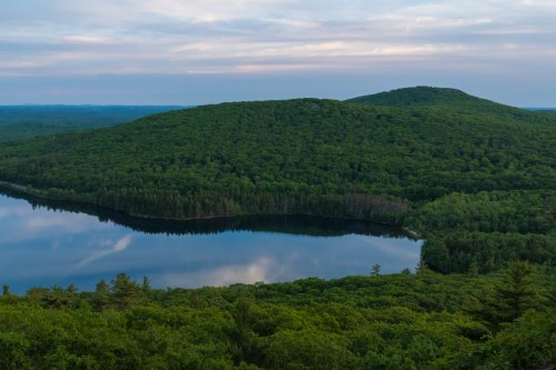 A serene landscape featuring a lush green hill reflected in a calm lake under a cloudy sky.