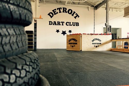 Interior of Detroit Dart Club featuring a logo on the wall, a wooden counter, and stacked tires in the foreground.