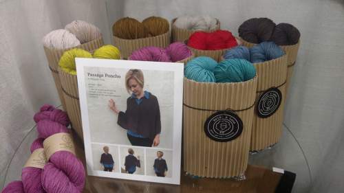 A display of colorful yarn skeins in cardboard containers, with a pattern guide for a poncho in front.
