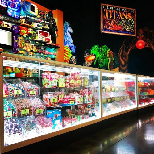 A colorful display of retro toys and candy in a vibrant arcade setting with a mural in the background.