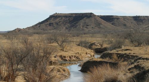 A serene landscape featuring a winding creek surrounded by dry grass and distant hills under a clear blue sky.
